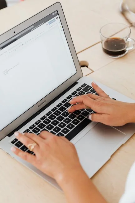 Hands using smartphone beside laptop with stock charts, showcasing digital trading.